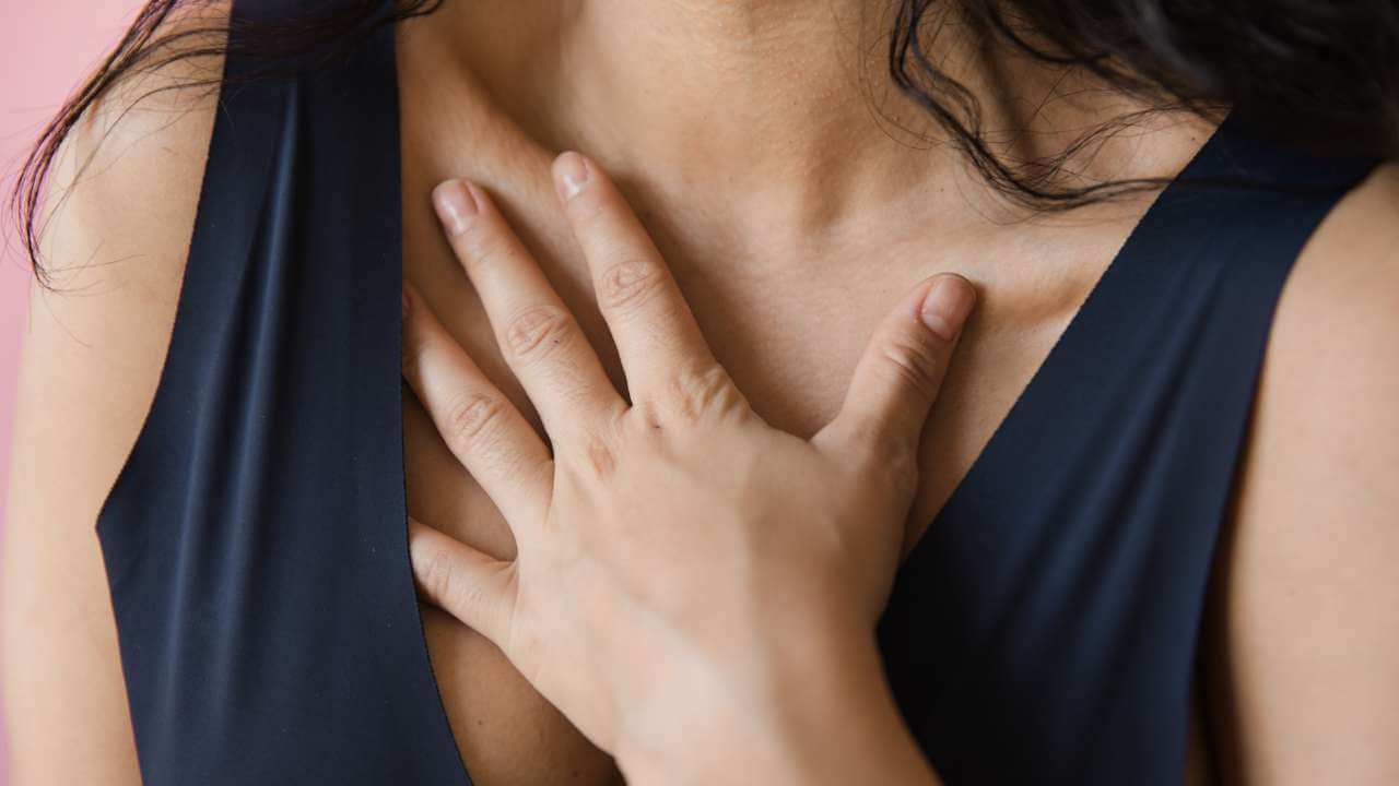 Closeup of a woman wearing a black sleeveless shirt, covering her chest acne with her left hand. 