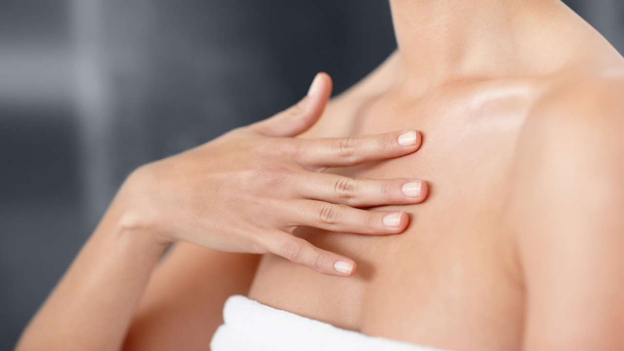 Closeup of a woman running her fingers over the smooth skin on her chest while wrapped in a white towel.