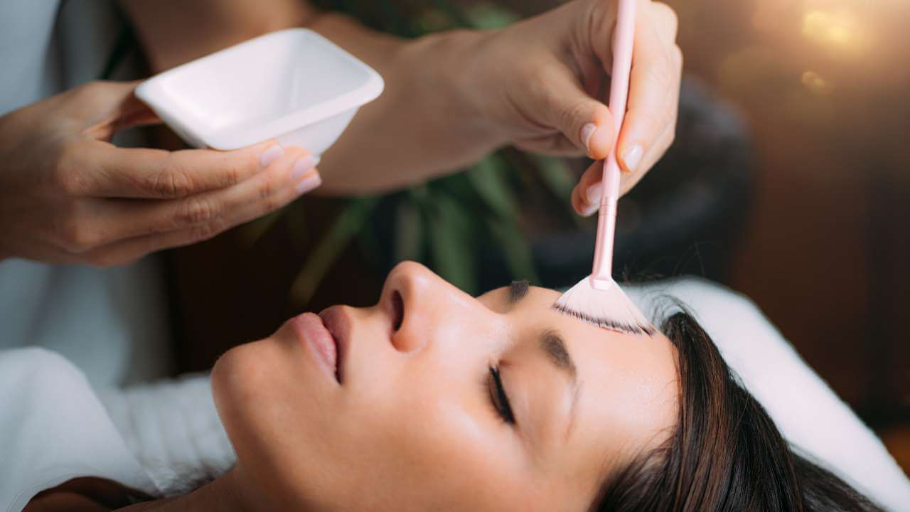 Esthetician treating post-inflammatory hyperpigmentation on a woman’s forehead with chemical peels applied with a brush.