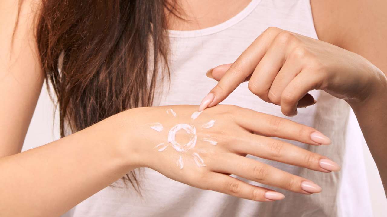 Woman shows how to apply sunscreen with zinc oxide and titanium dioxide to the back of her hand to prevent liver spots. 