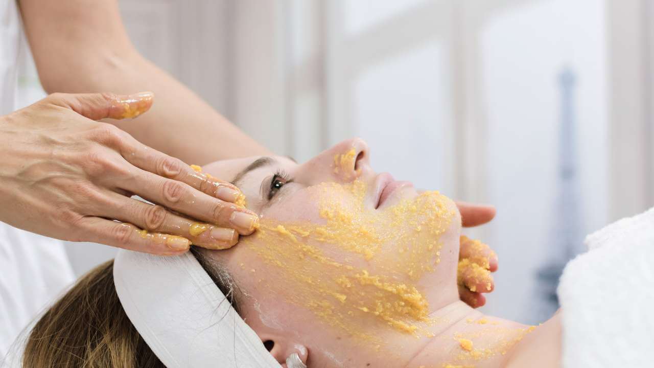 Esthetician treating hyperpigmentation with home remedies, using her hands to gently massage turmeric on a woman’s face.