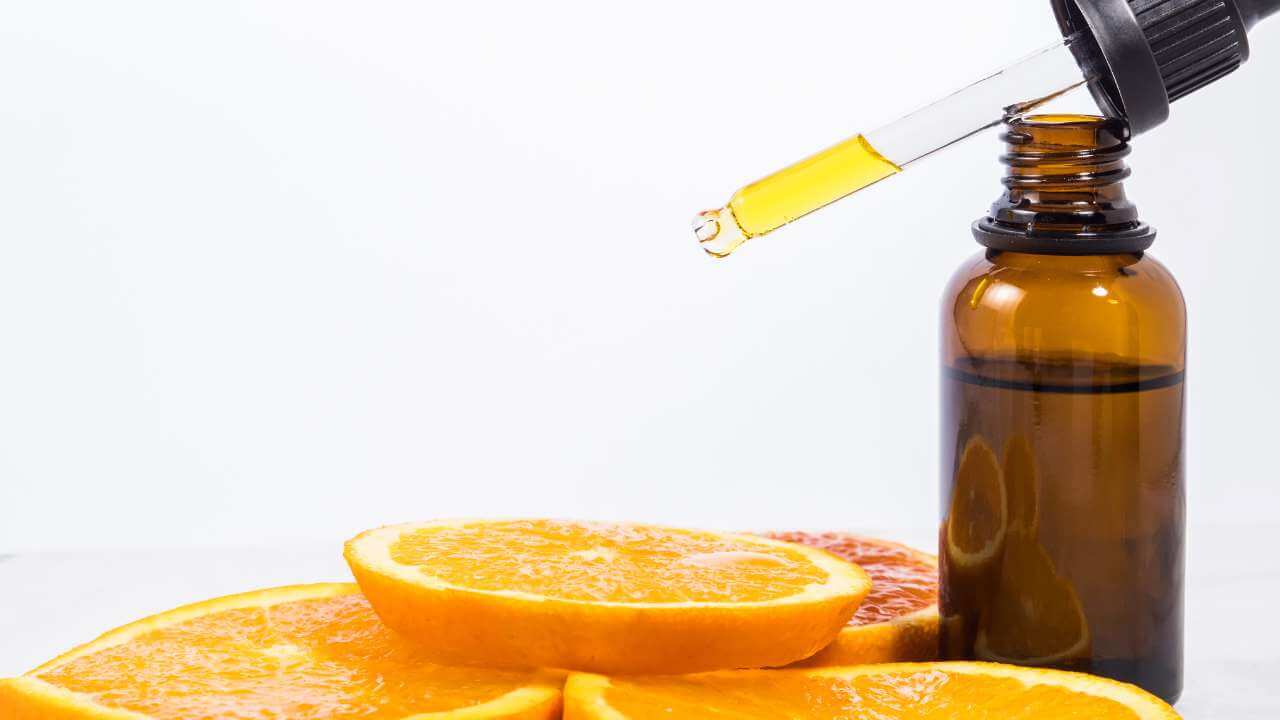 Small dropper of vitamin c serum used to combat hyperpigmentation, on top of an amber bottle next to 4 orange slices.