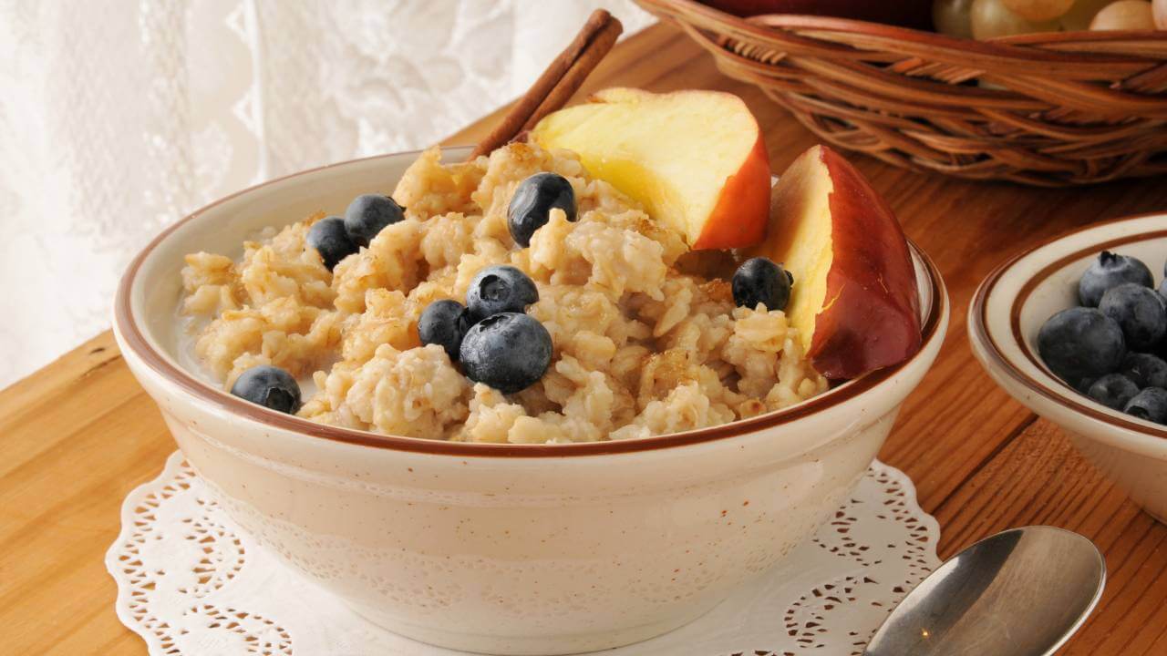 A bowl of oatmeal with added collagen, blueberries, and apples on top.