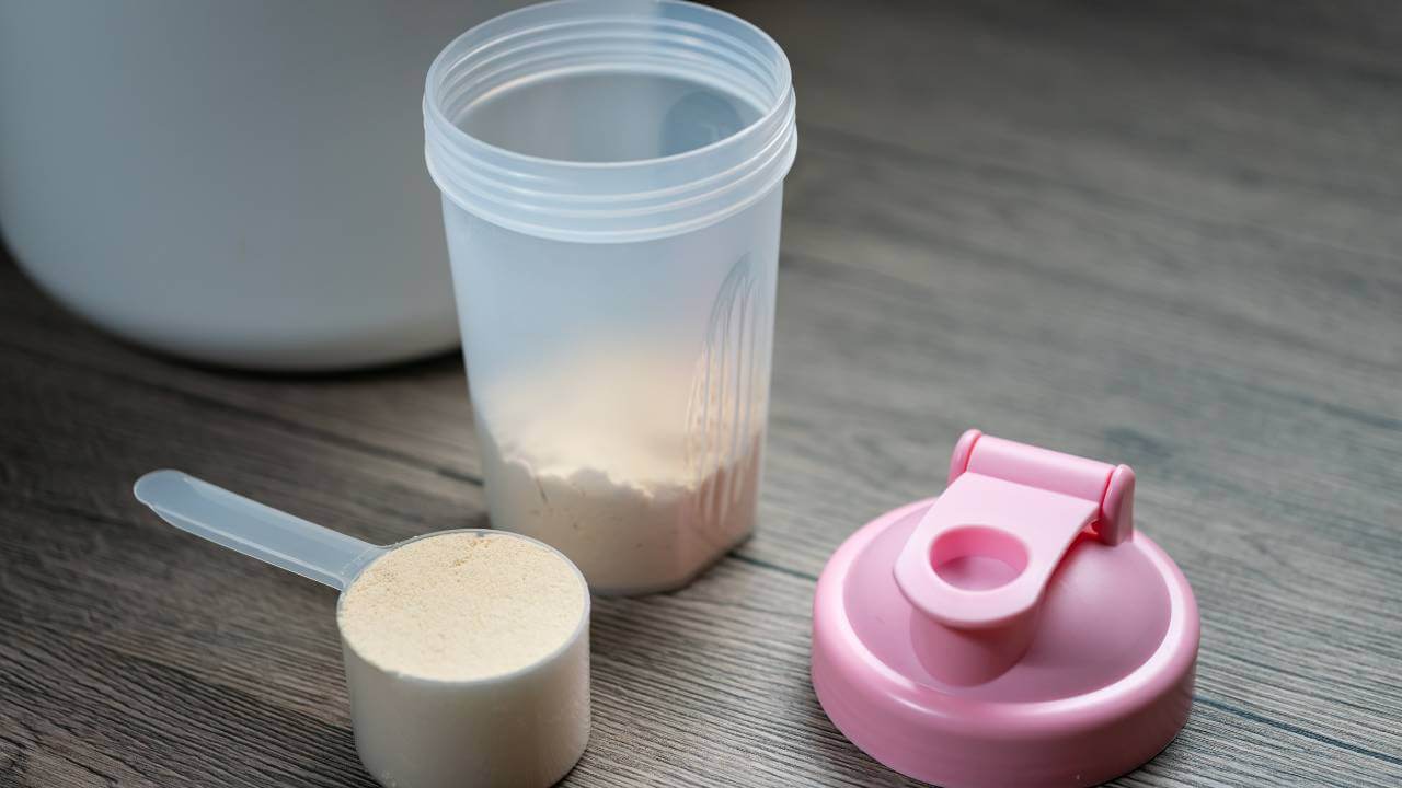 Scoop of protein powder next to a shaker bottle used to prevent collagen powder from clumping for the desired consistency.