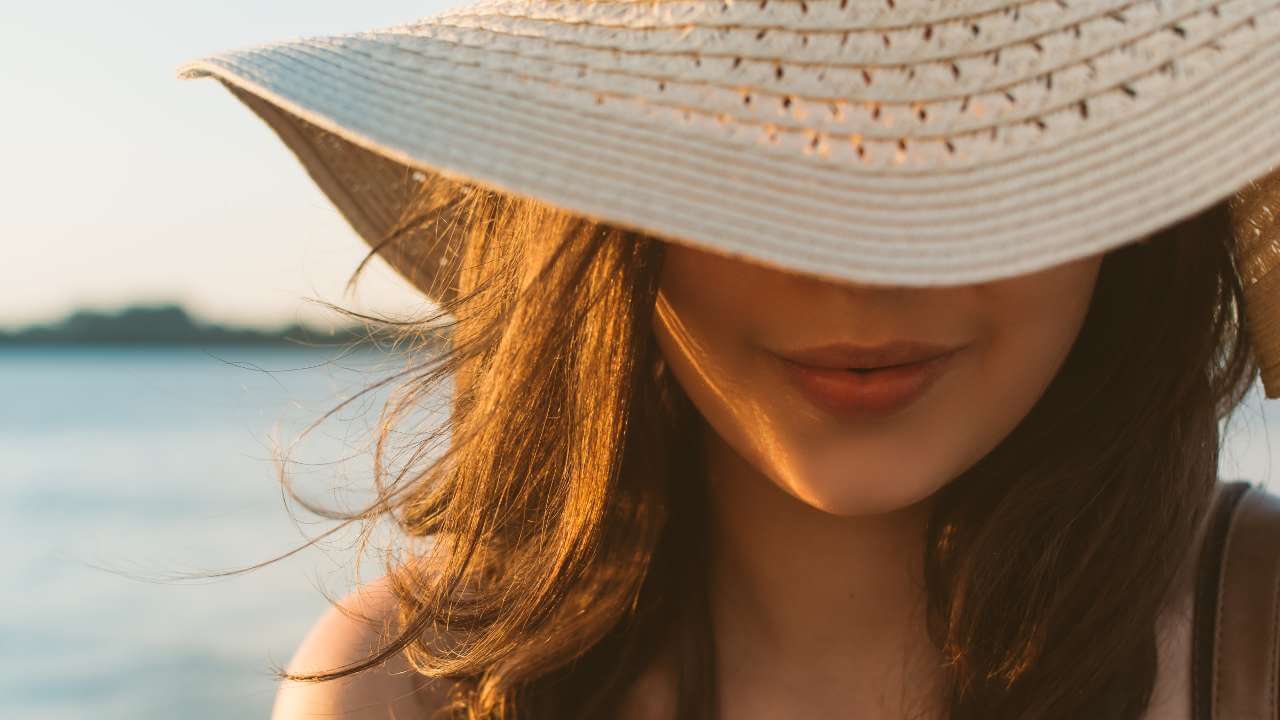 Woman wearing a wide brimmed hat outdoors to prevent sun spots by shielding her face from intense sun exposure.