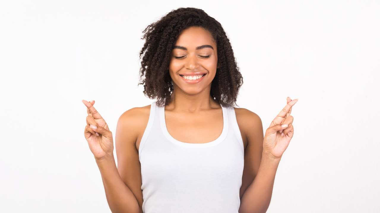 Young black woman smiling with eyes closed and fingers crossed, hoping to learn how to help fade hyperpigmentation.