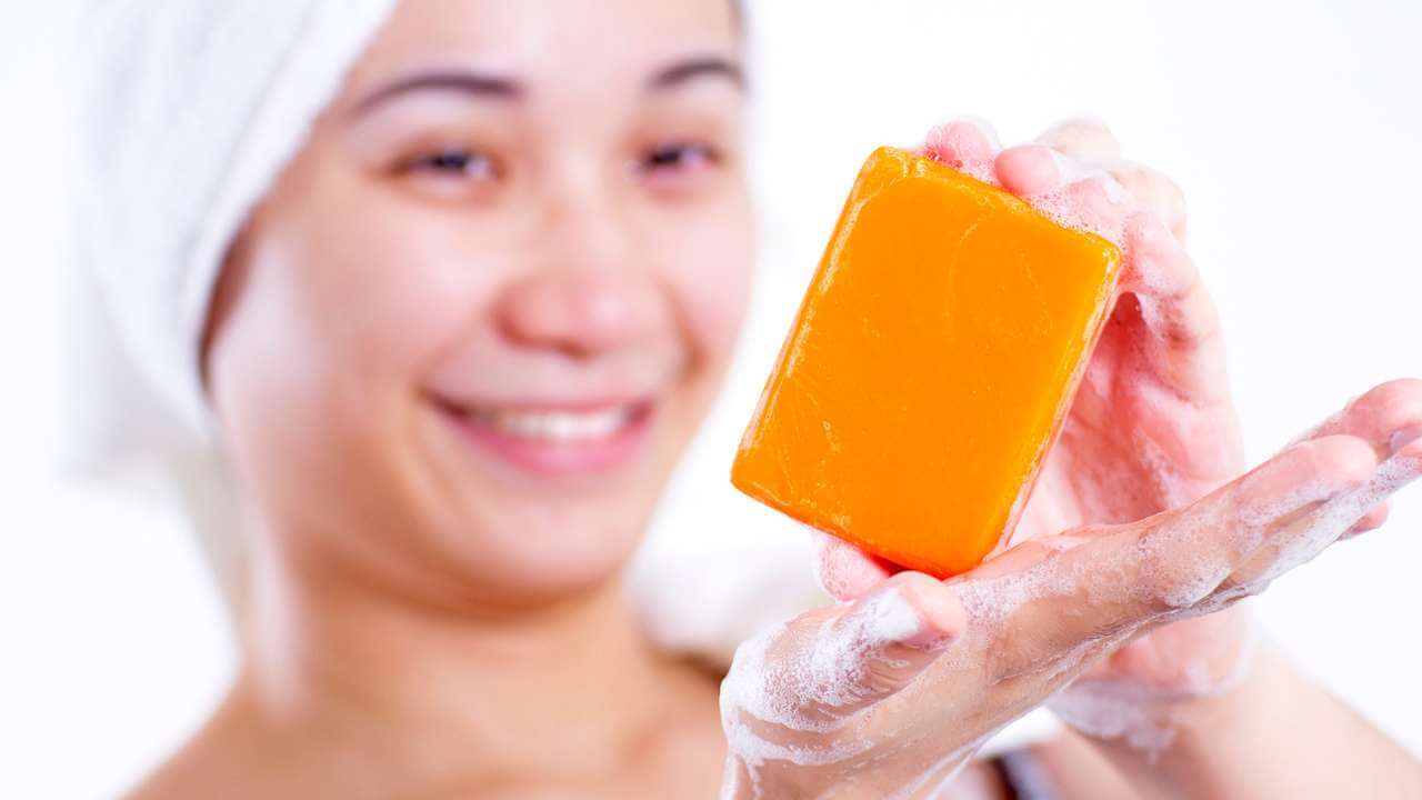 Happy Asian woman with soapy hands holding a bar of kojie san skin lightening soap with naturally derived ingredients. 