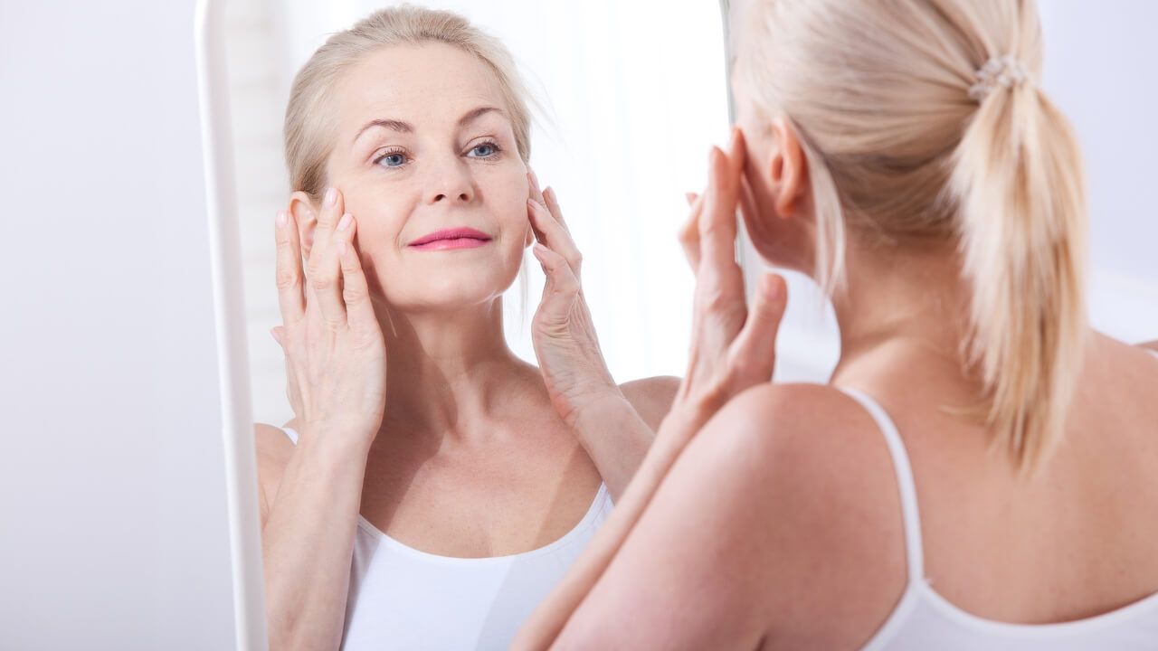 Middle-aged woman looking into a mirror, touching her face after using collagen supplements in her skincare routine.