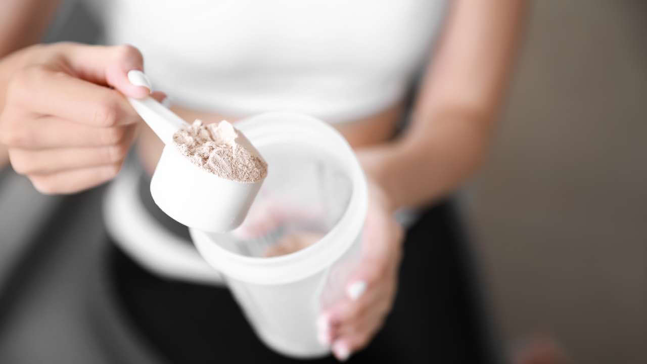 Woman adding collagen powder to a shaker bottle for an extra boost of amino acids after resistance training.